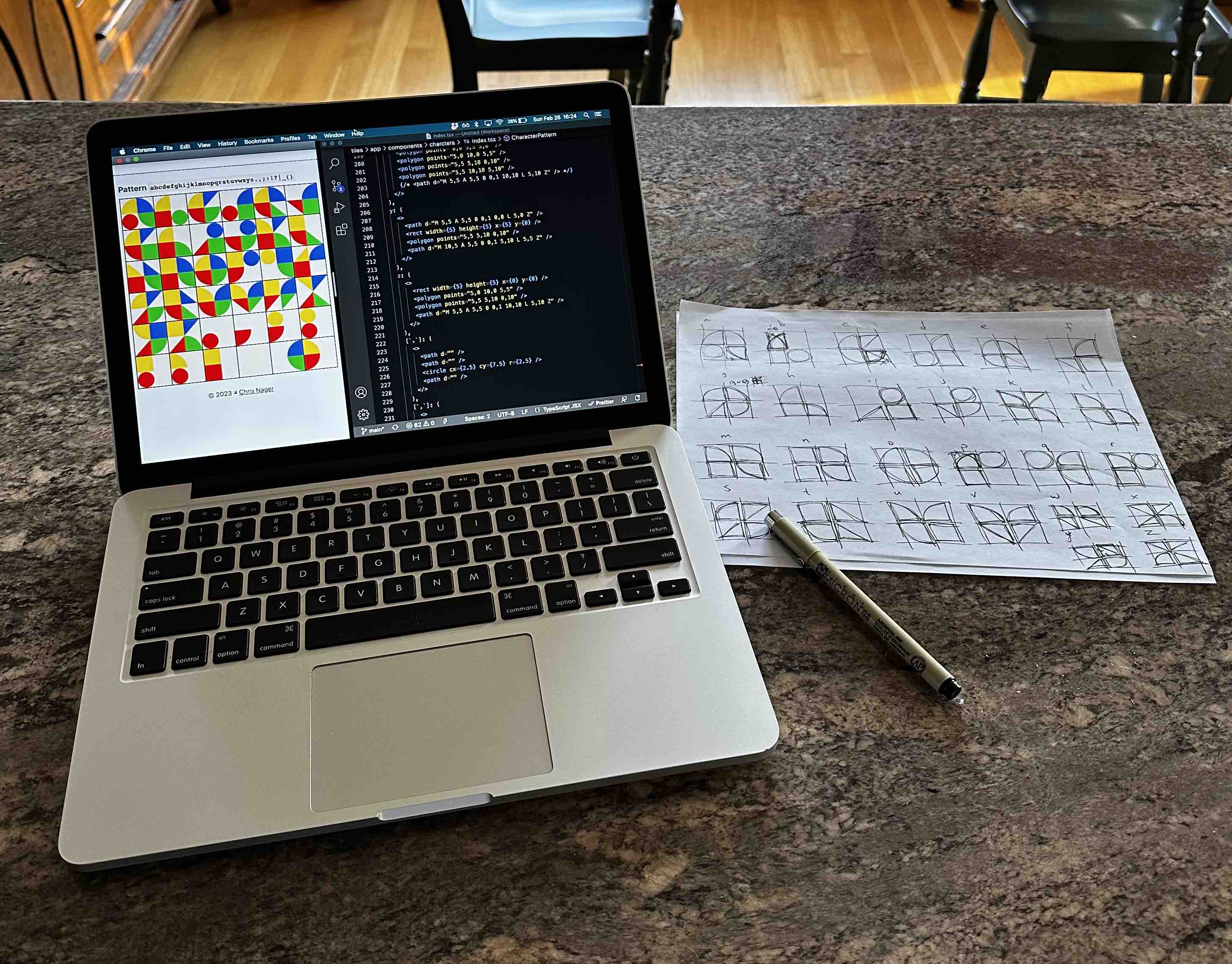 Computer displaying the in-progress Tiles site and a code editor, with a piece of paper next to it with sketches of the geometric Tiles typeface